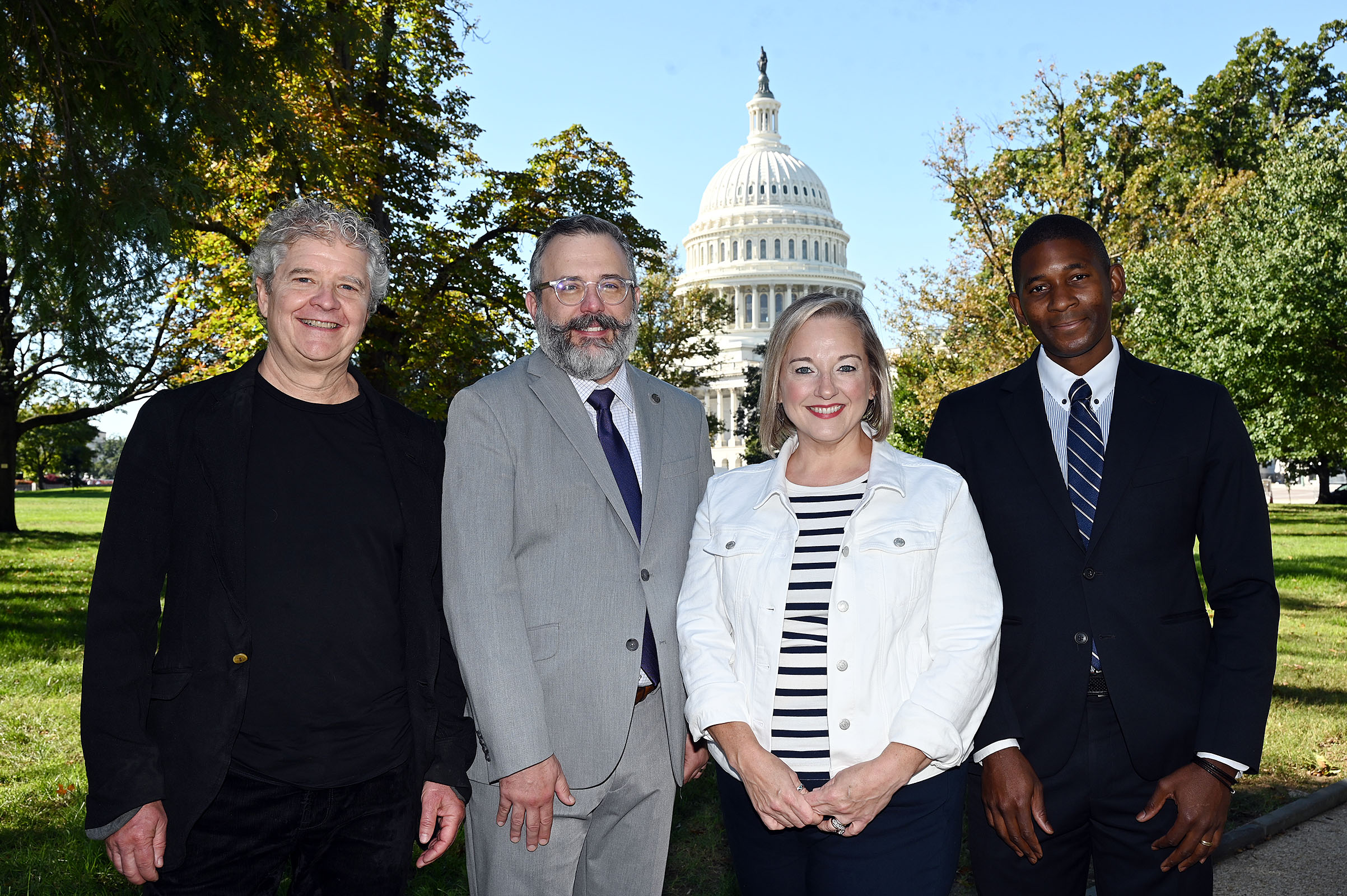 4 individuals standing for a photo with the Capitol in the background.