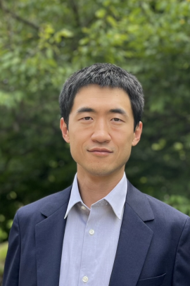 Yingjian with a blue suit jacket and light blue dress shirt against trees backdrop